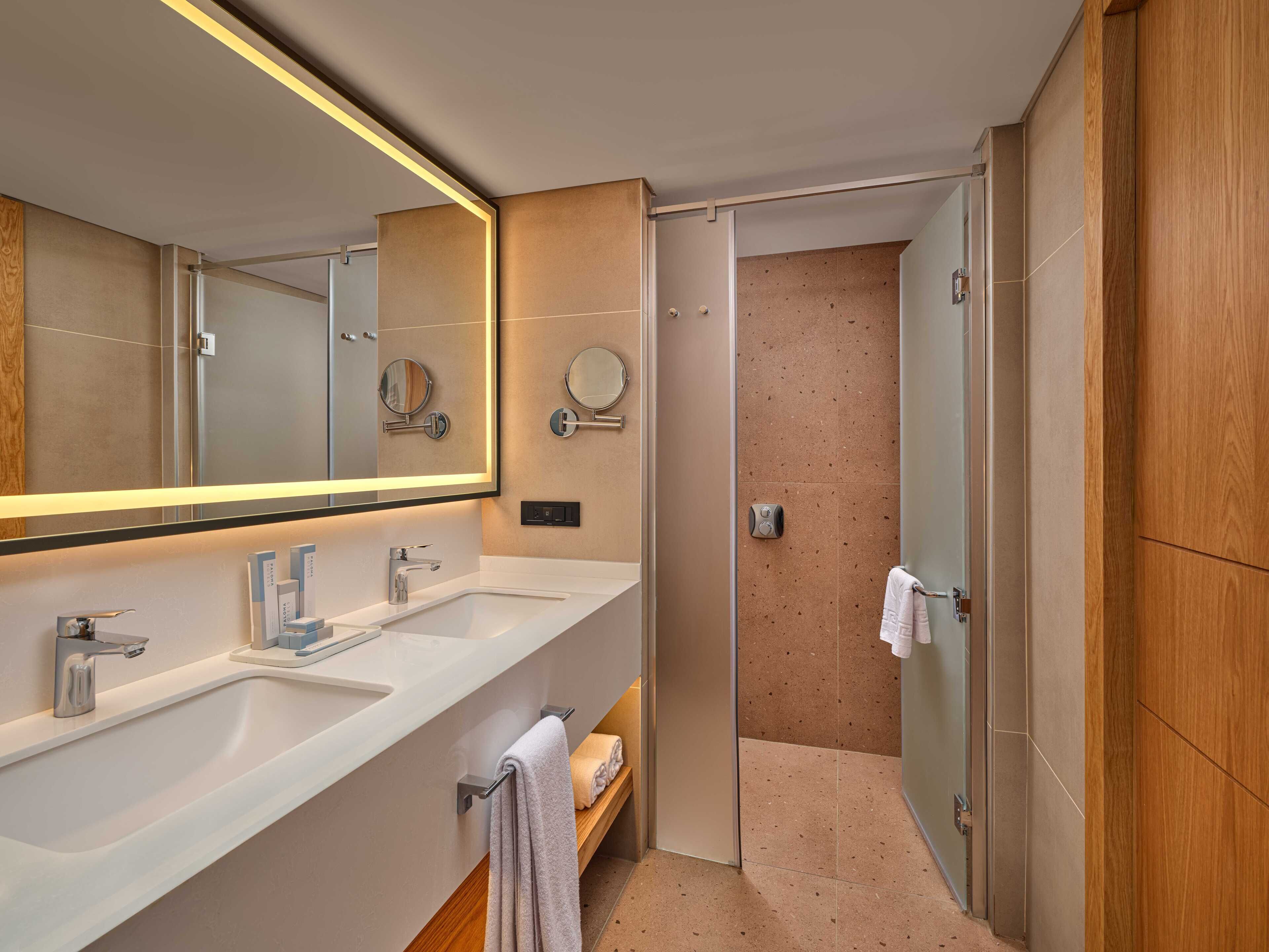 A modern bathroom with two sinks, a large mirror, and a shower area.