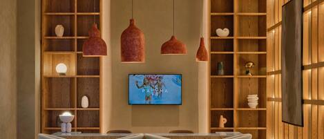 A modern bar area with wooden shelving, pendant lighting, and a flat-screen TV.