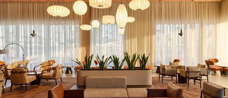 Un vestíbulo amplio con diseño moderno, que presenta una zona de estar central con sofás y sillones, rodeada de plantas en macetas.