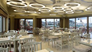 Un comedor con varias mesas y sillas, luces de techo circulares y grandes ventanales que ofrecen vista a la ciudad.