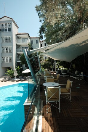 Un espace aménagé au bord de la piscine, avec une terrasse en bois, des chaises longues et un coin salon abrité.