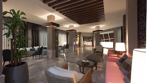 Un vestíbulo amplio con diseño moderno, que incluye una zona de estar con sofás y sillones, una gran planta en maceta y un ambiente luminoso.