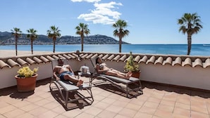 Una terraza con tumbonas con vistas a una playa y palmeras.