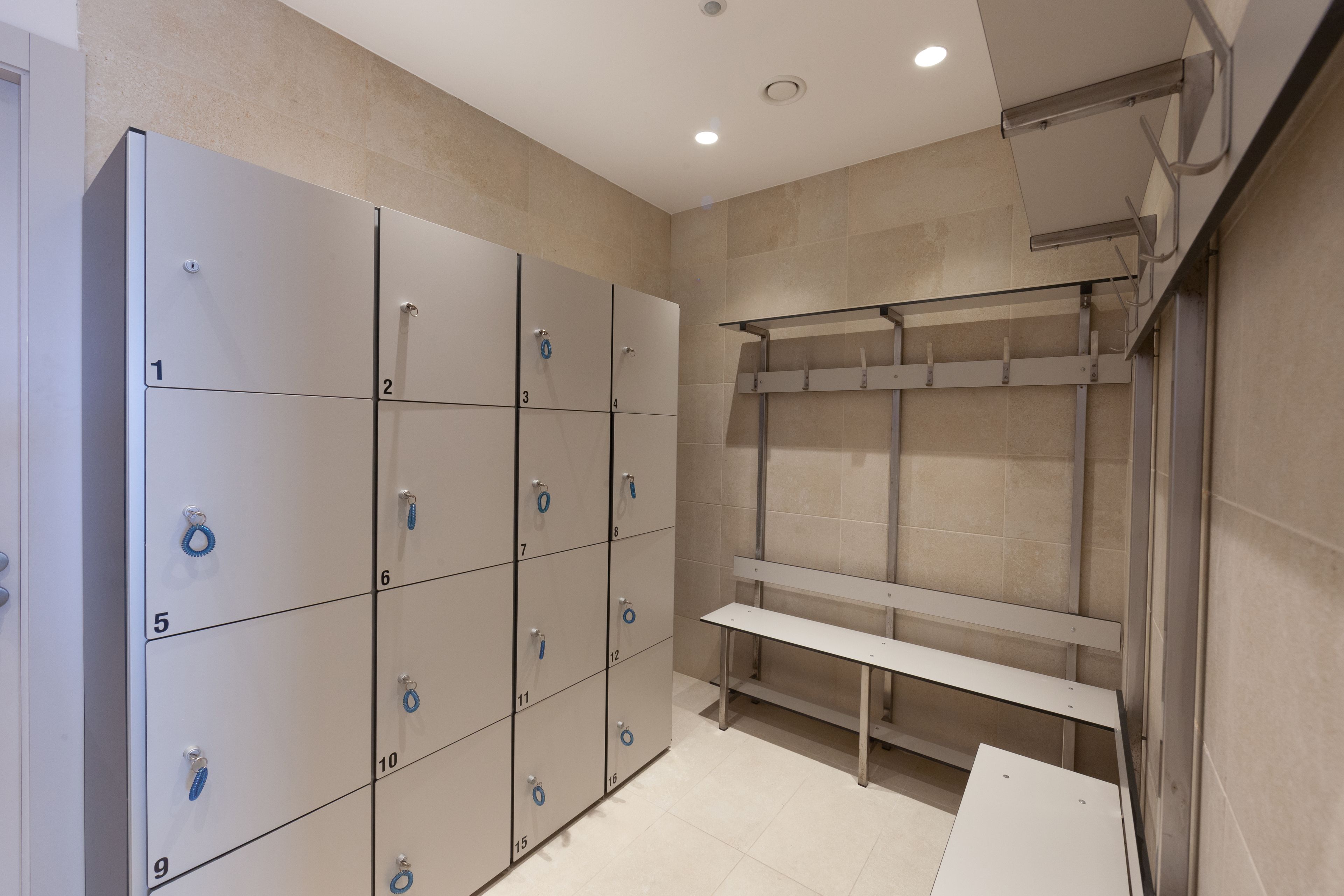 Een rij getallenloten met nummers 1 tot 16, een bankje en een douchegedeelte met een glazen cabine.