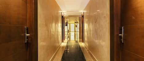 A corridor with wooden doors and a black marble floor leading to a bright, well-lit room with a large window.