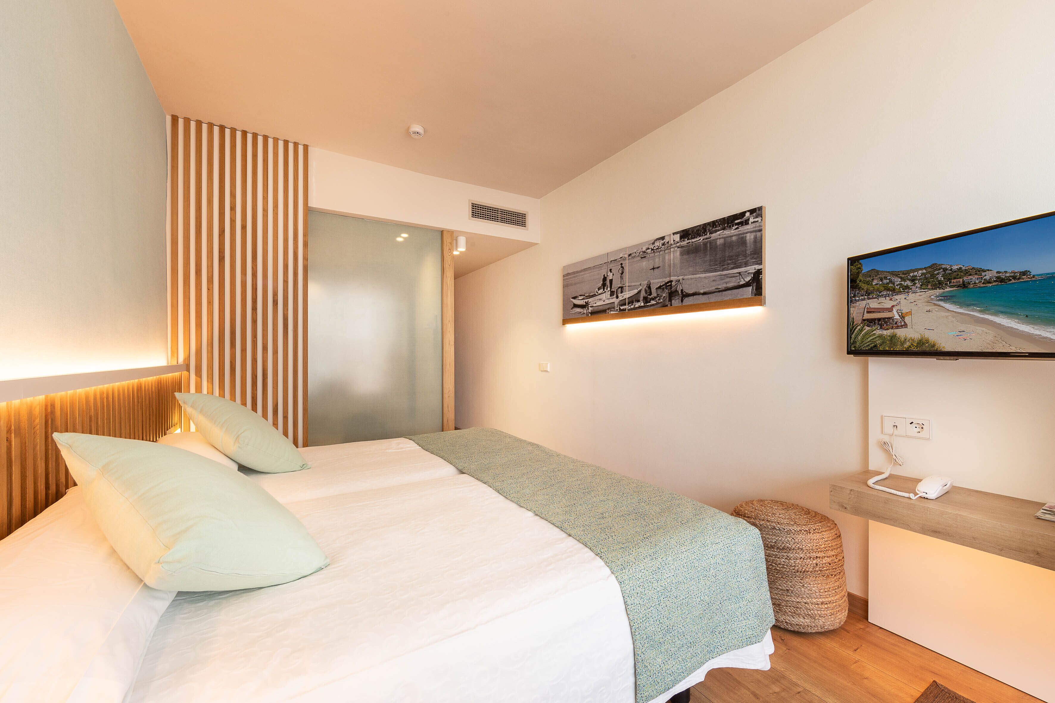 A modern bedroom with a bed, a wooden headboard, a wall-mounted TV, and a beach view painting.