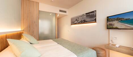 A modern bedroom with a bed, a wooden headboard, a wall-mounted TV, and a beach view painting.