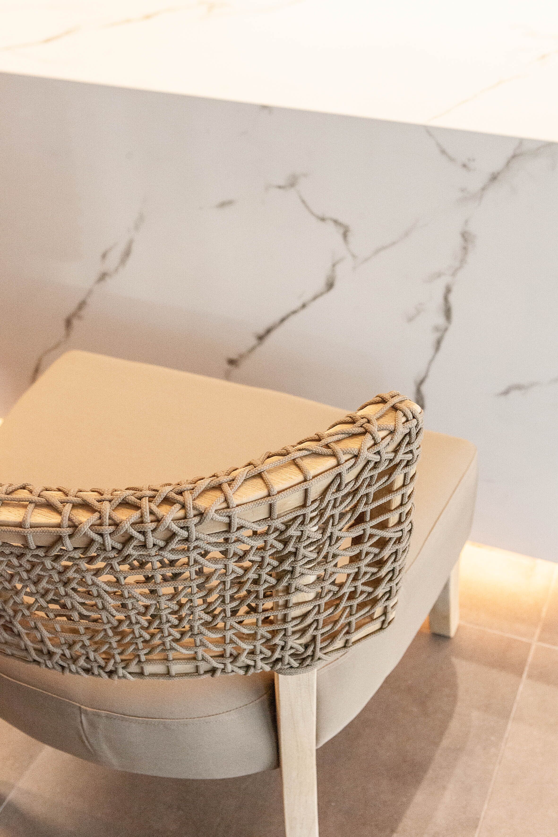 A chair with a woven backrest and a cushioned seat, placed against a marble wall.
