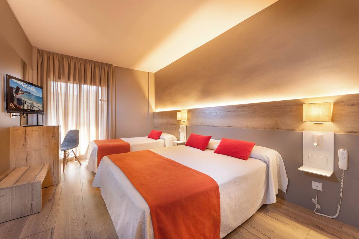 A hotel room with two beds, a TV, a desk, and a chair.