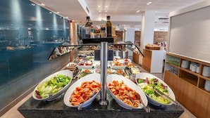 Montaje de bufé con diversas opciones de comida, incluyendo ensaladas y platos calientes, sobre una encimera de granito en un entorno moderno de hotel.