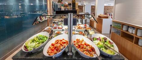 A buffet setup with various food items including salads and cooked dishes, arranged on a granite countertop in a modern hotel setting.