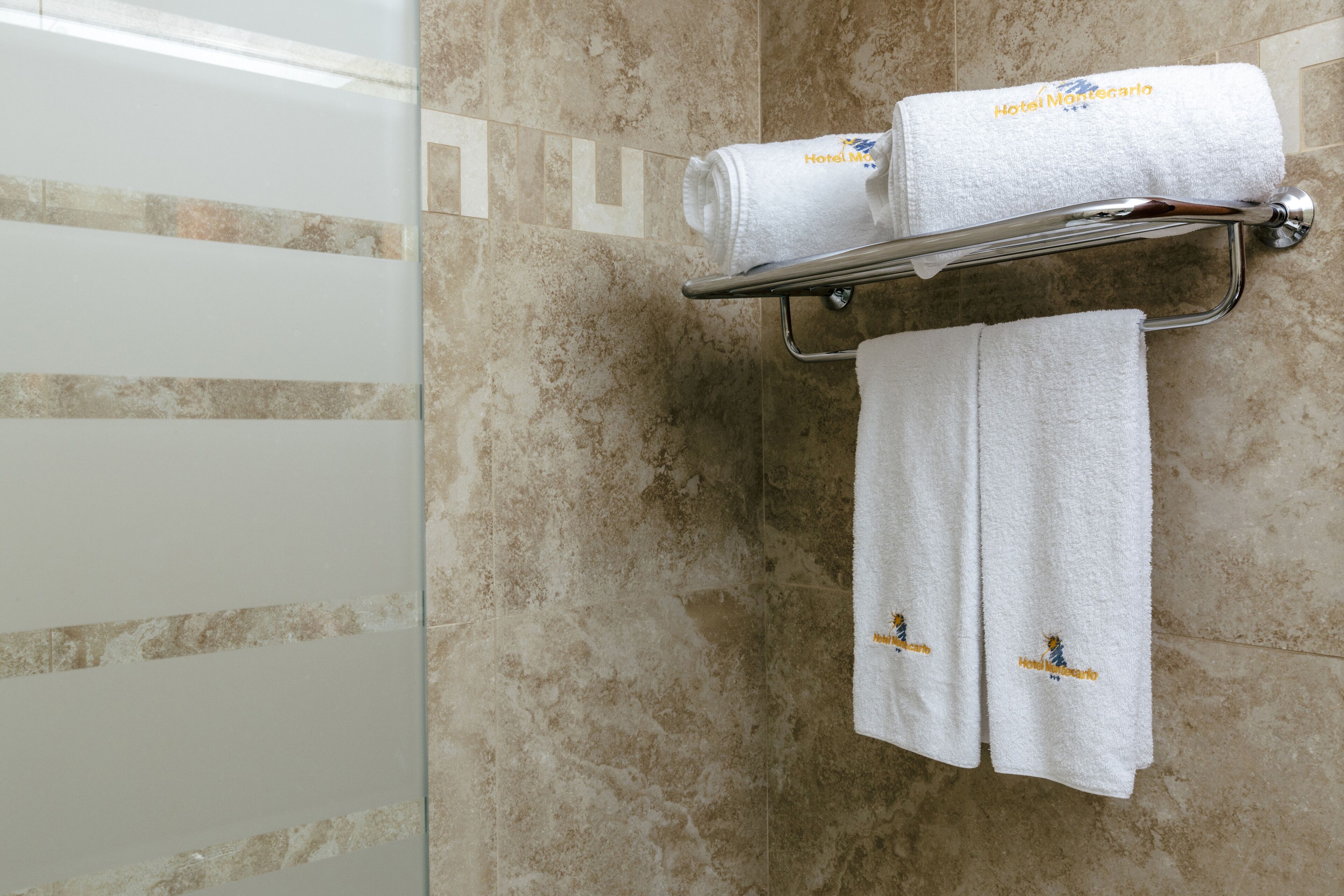 A bathroom with a glass shower door, a towel rack with two white towels, and a wall with a geometric pattern.