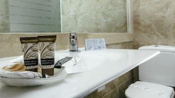 Un baño con un lavabo blanco, dos botellas de gel de ducha y champú, un afeitador y una caja de pañuelos.