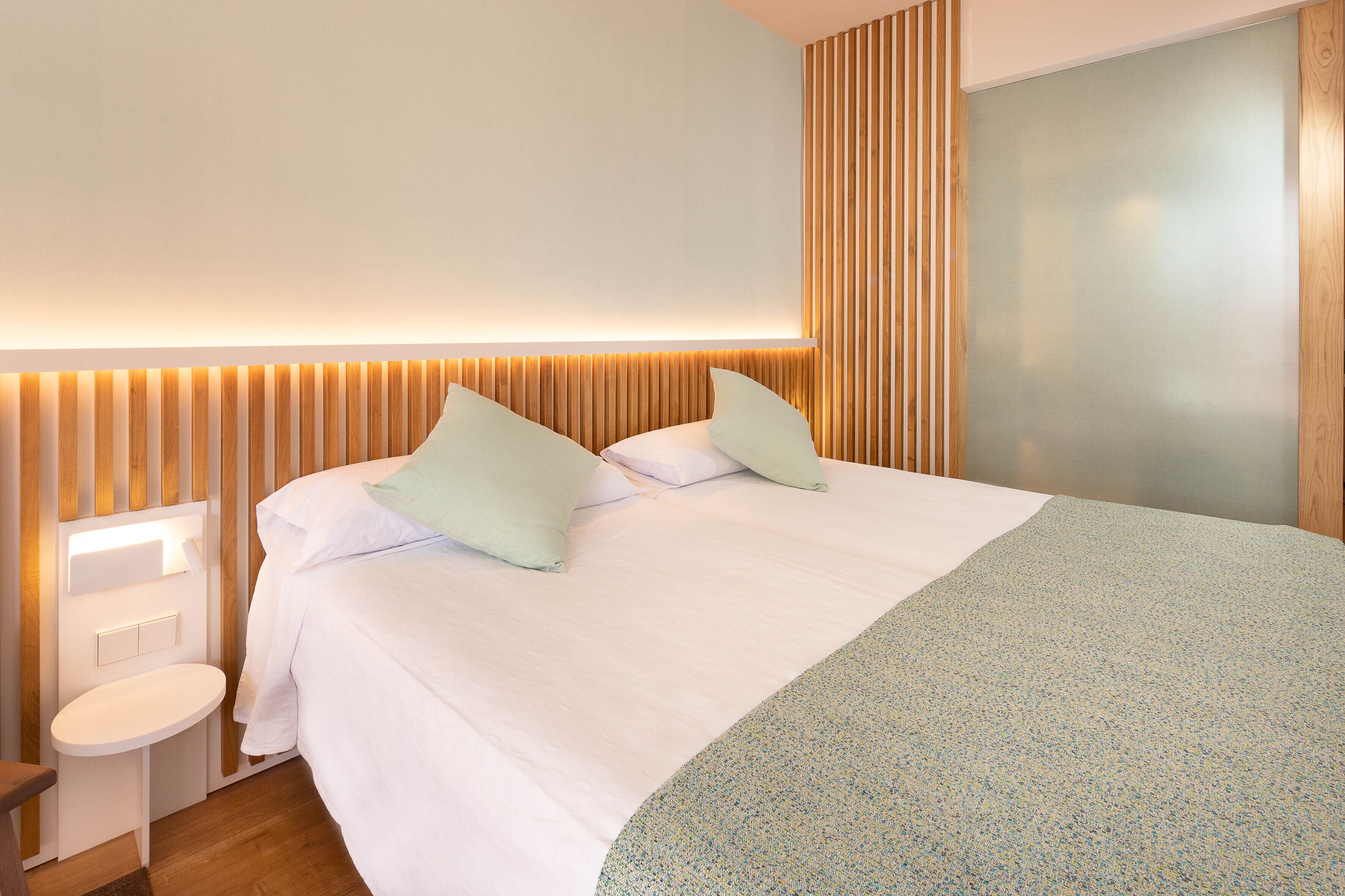 A modern hotel room with a large bed, a bedside table, and a wall-mounted light fixture.
