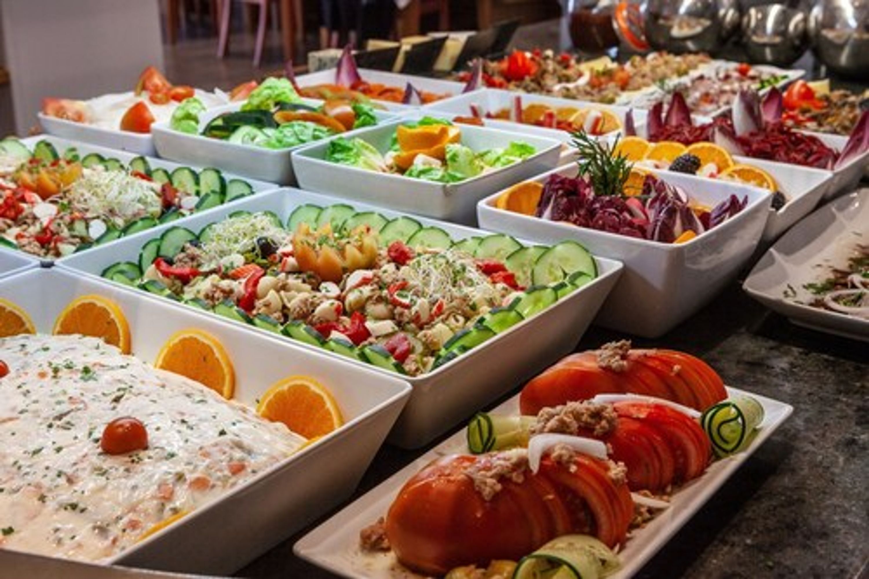 A buffet with various dishes including salads, fruits, and a creamy dish with a cherry on top.