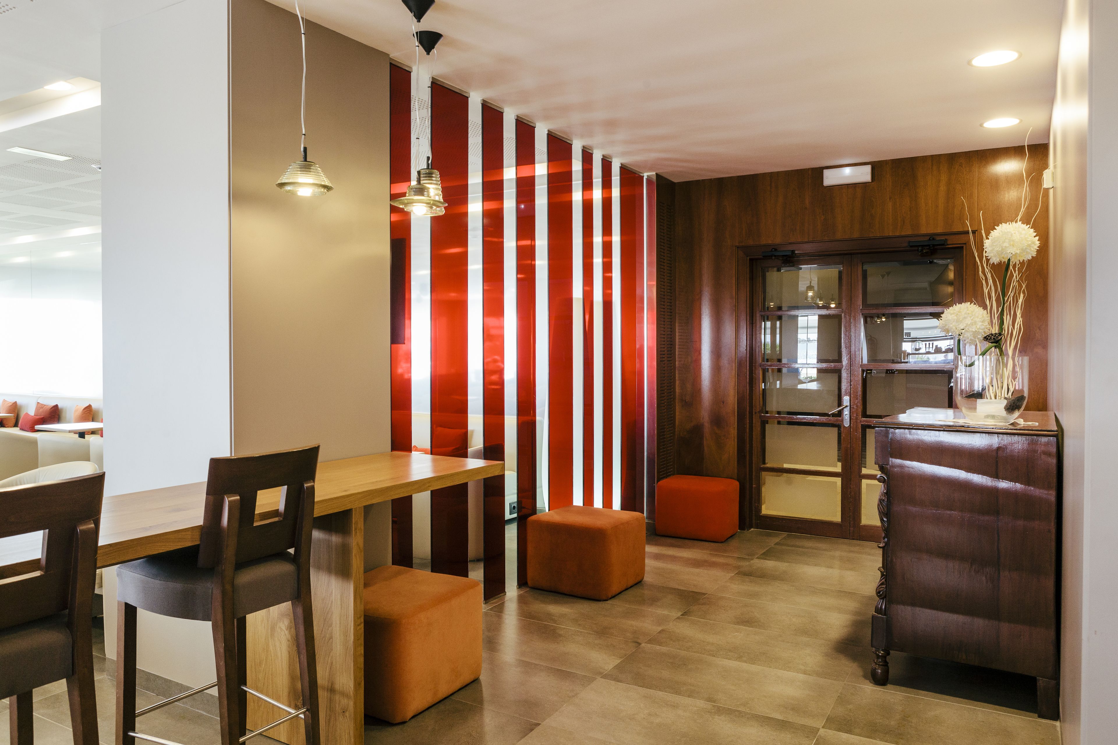 Un comedor moderno con mobiliario de madera, un separador a rayas rojas y blancas, y un aparador con un jarrón de flores.