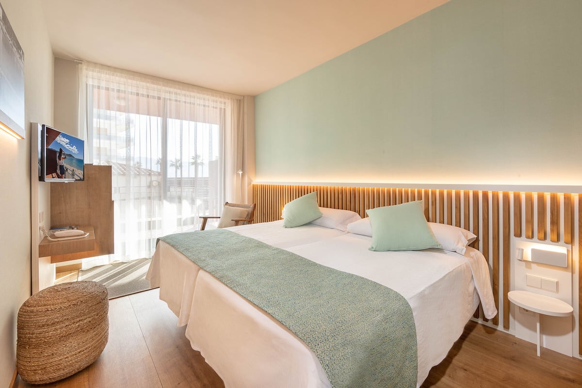 Ein modernes Hotelzimmer mit einem großen Bett, einem Nachttisch, einem an der Wand befestigten Fernseher und Blick ins Freie.