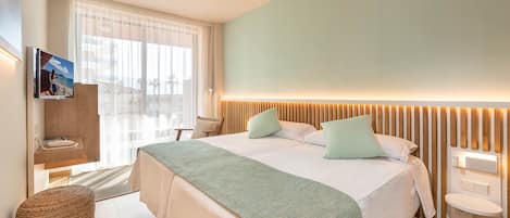 A modern hotel room with a large bed, a bedside table, a wall-mounted TV, and a view of the outdoors.