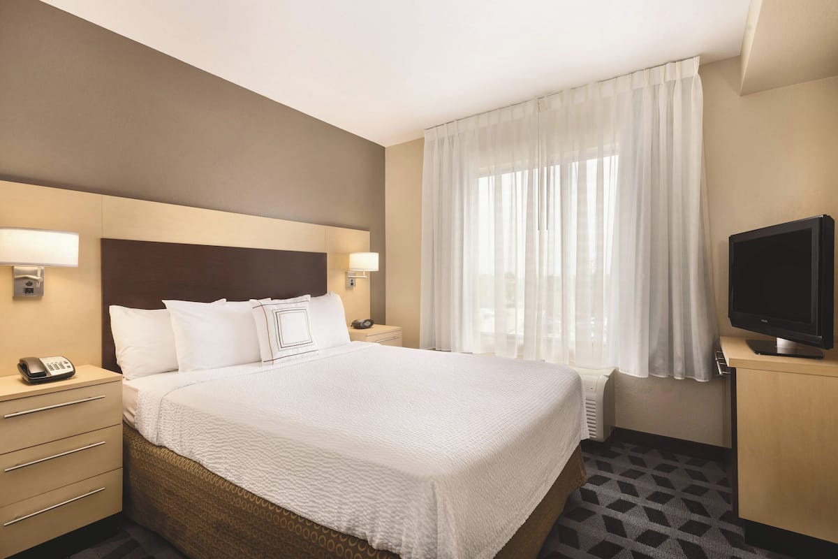 Habitación de hotel con una cama grande, televisión, lámpara de noche, teléfono y ventana con cortinas.