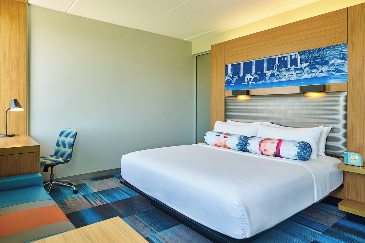 A hotel room with a large bed, a desk, a chair, and a painting on the wall.