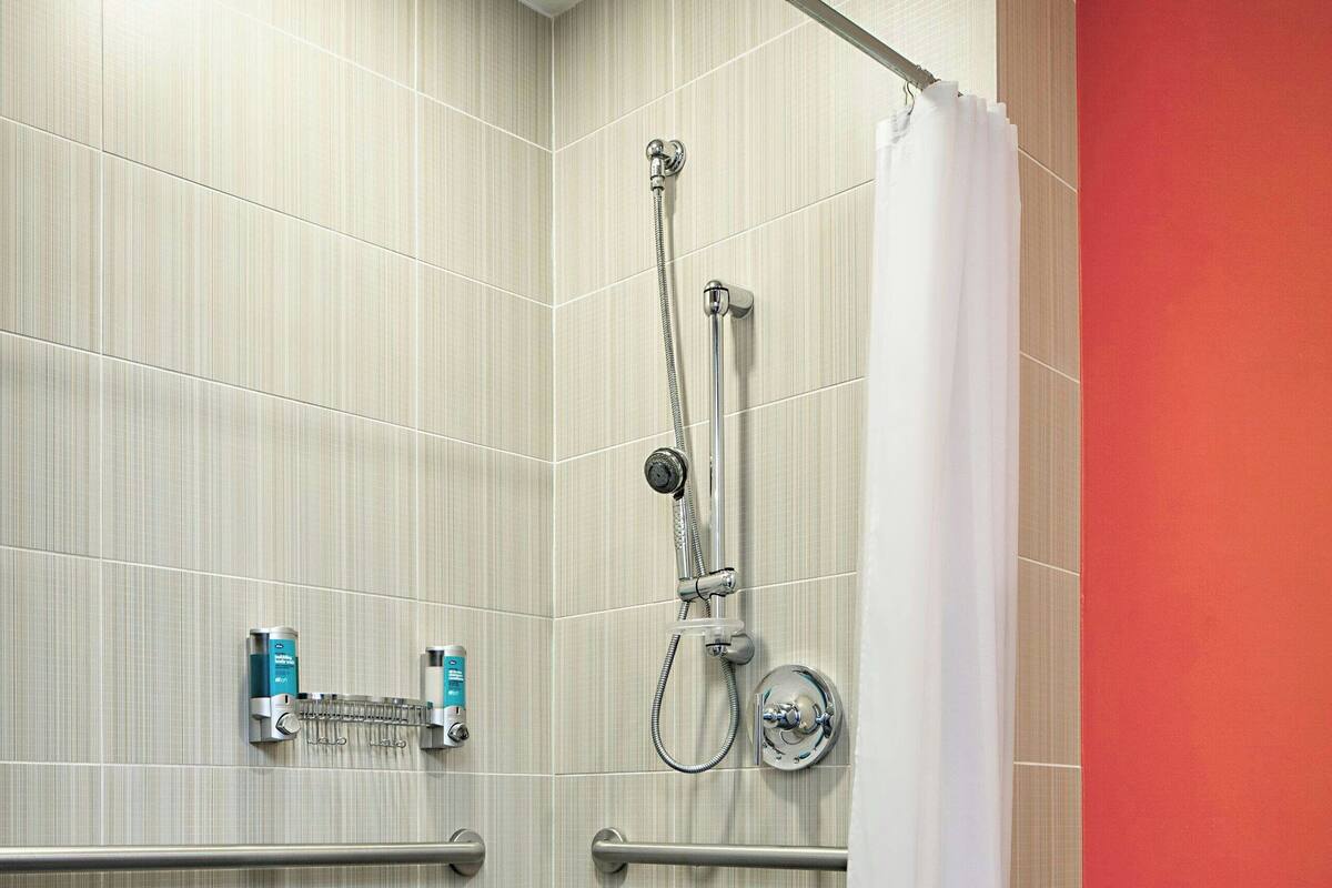 A shower area with a handrail, a showerhead, and a curtain.