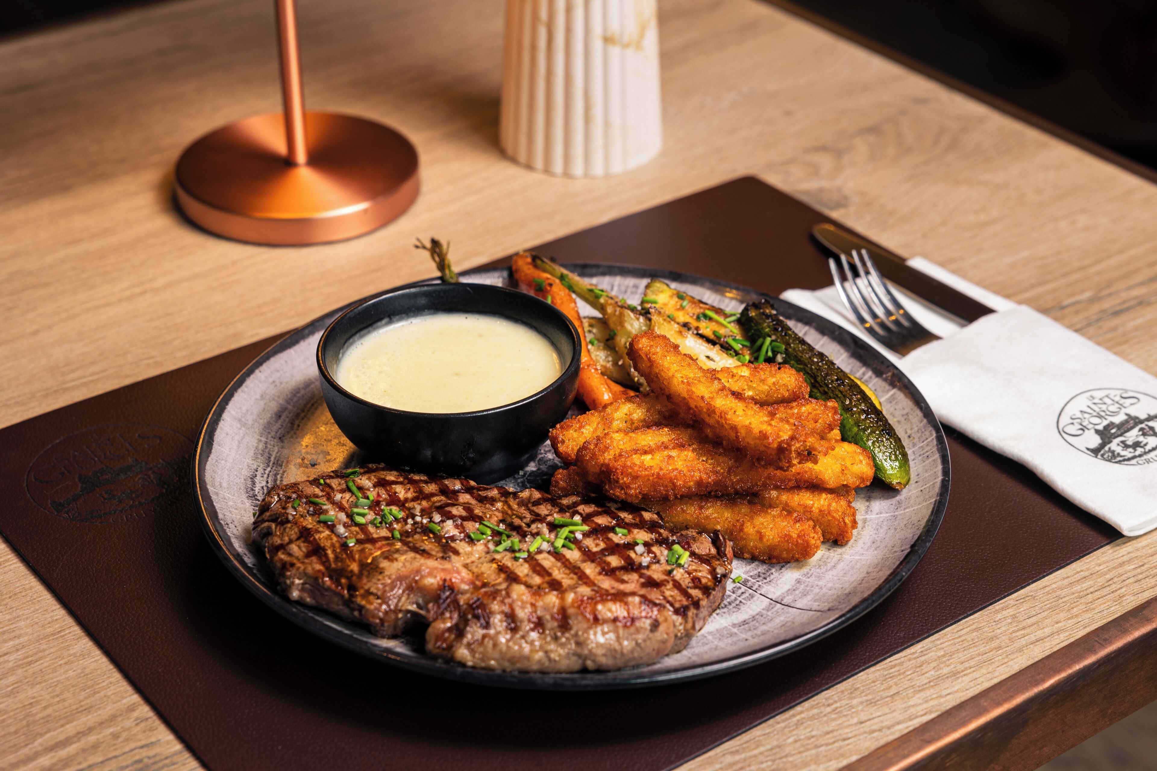 Un plato con un filete a la parrilla, acompañamientos fritos y salsa para mojar sobre una mesa de madera.