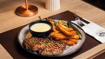 Un plato con un filete a la parrilla, acompañamientos fritos y salsa para mojar sobre una mesa de madera.