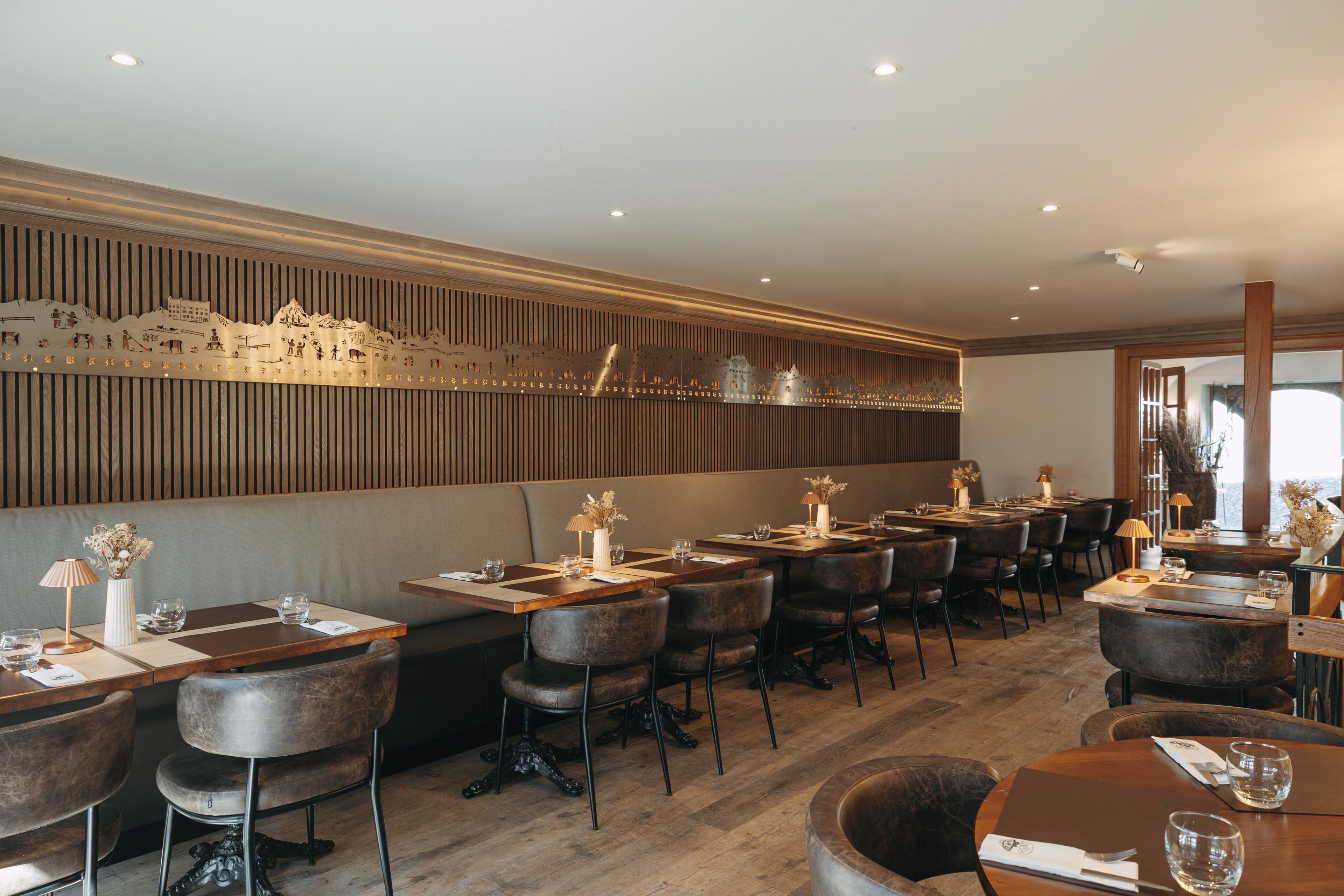 A restaurant with wooden tables and chairs, a decorative wall, and recessed lighting.