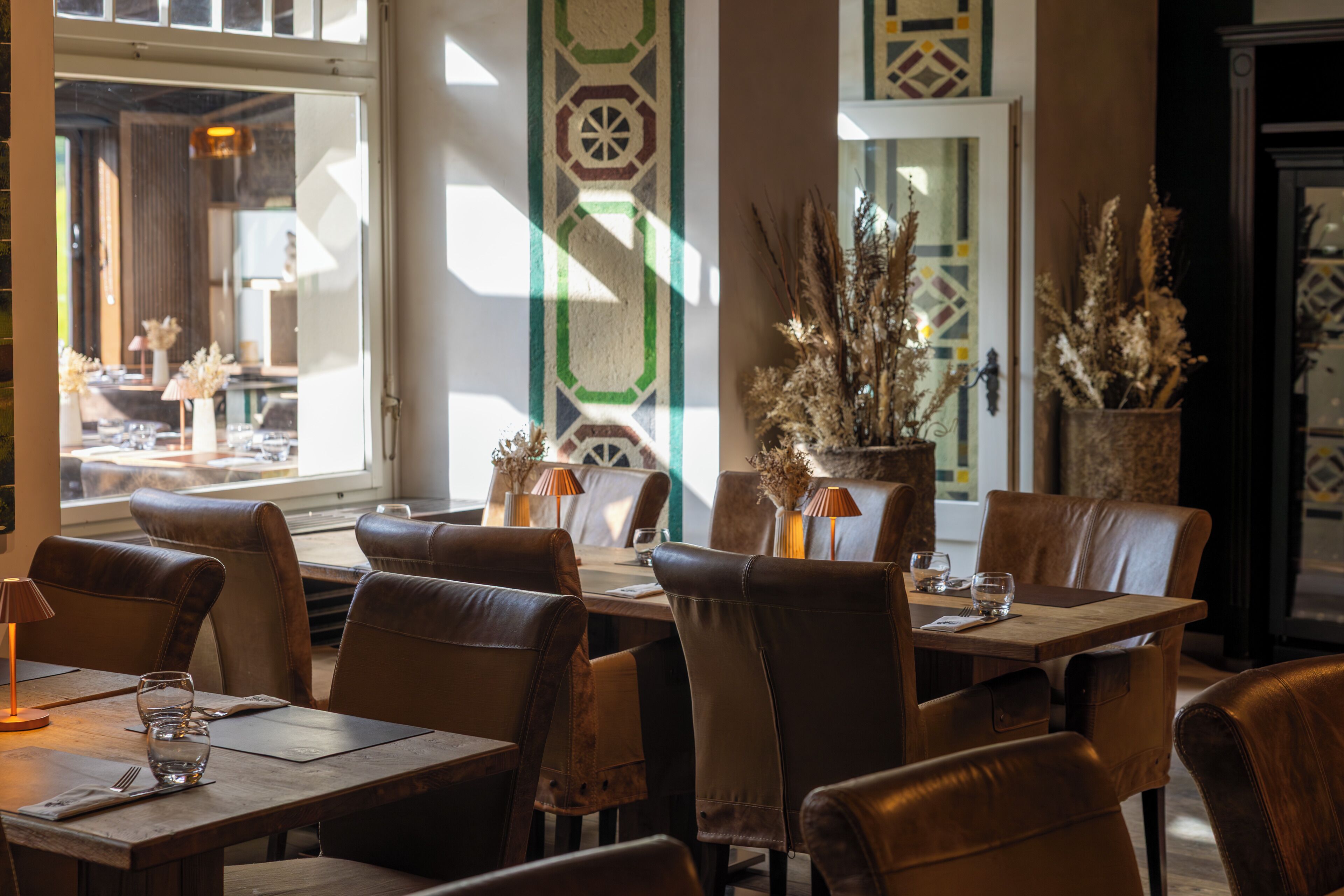 L’intérieur d’un restaurant, avec des fauteuils en cuir, des tables en bois et des plantes en pot.
