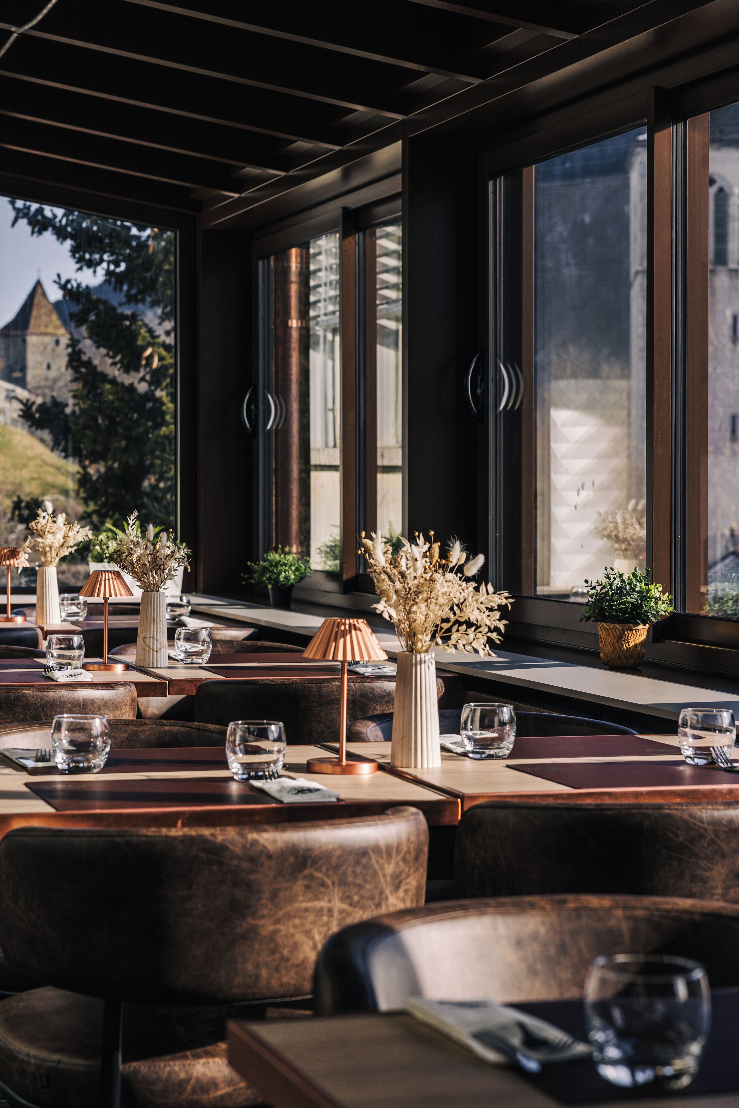 A restaurant with leather seating, tables set with glasses and cutlery, and decorative plants.