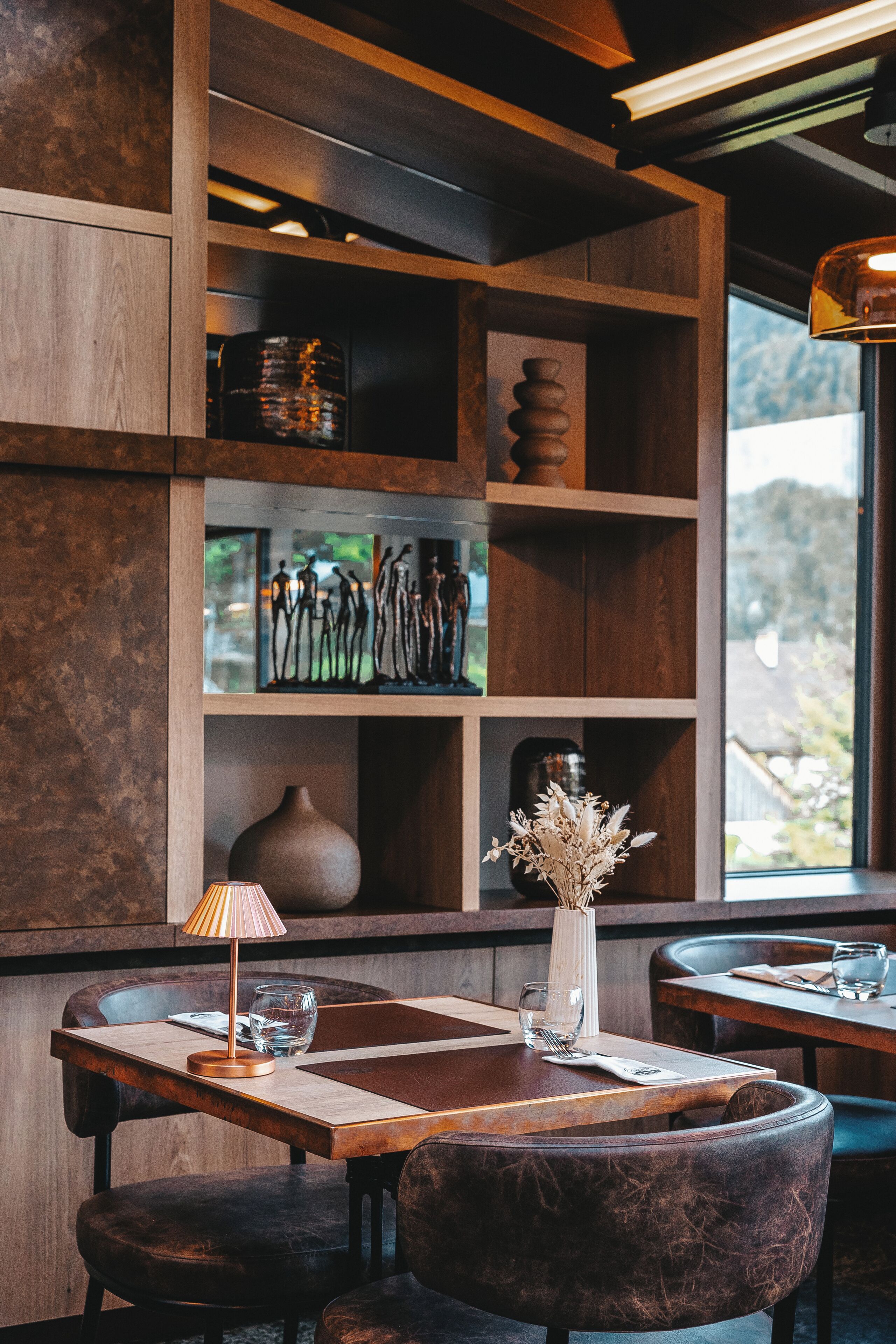 A restaurant interior with wooden shelves, a vase with dried flowers, and a table with chairs.