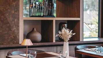 A restaurant interior with wooden shelves, a vase with dried flowers, and a table with chairs.
