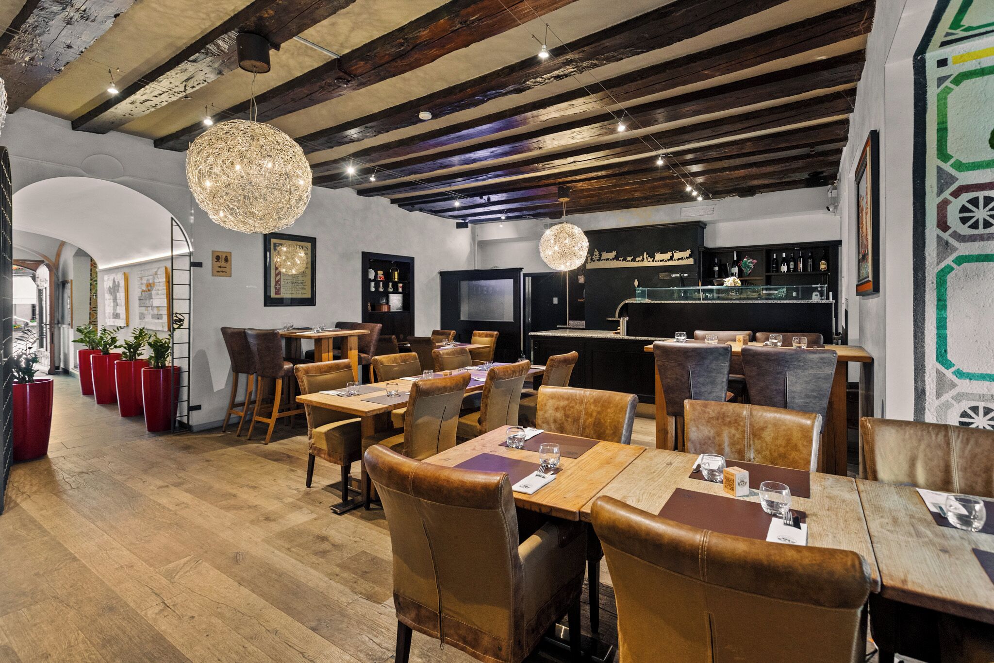 Un restaurante con mesas de madera y sillas de cuero, una zona de bar y una lámpara de araña moderna.