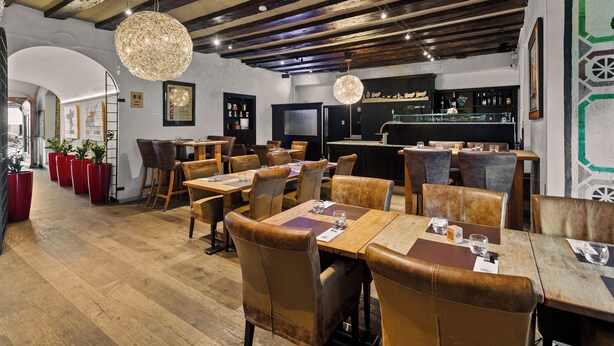 Un restaurante con mesas de madera y sillas de cuero, una zona de bar y una lámpara de araña moderna.