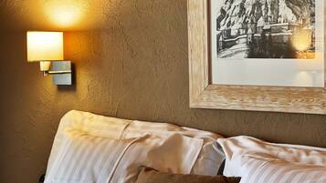 Una cama con ropa de cama a rayas y una almohada escocesa, un cuadro con una escena de montaña y una lámpara de pared.