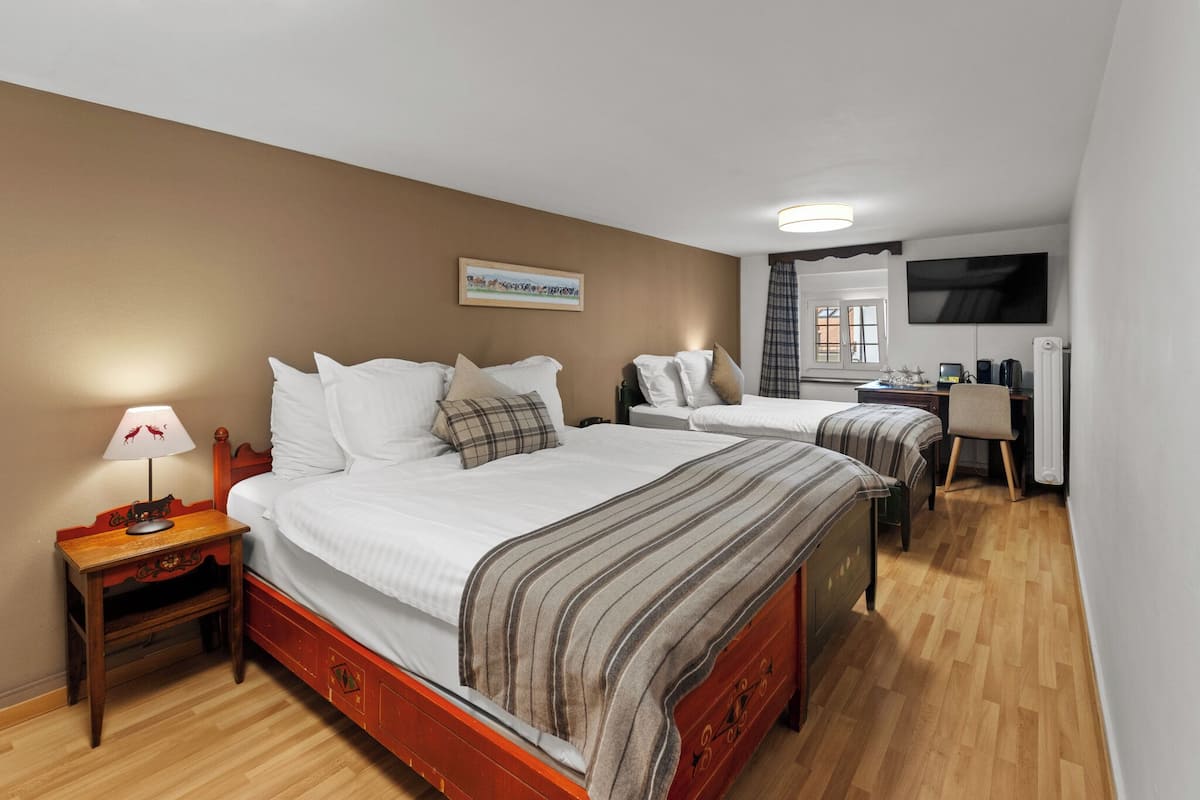 A hotel room with two beds, a desk, a television, and a lamp.