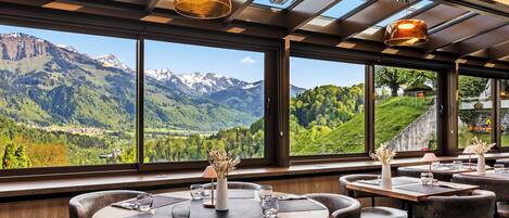 A restaurant with round tables and chairs, large windows with a mountain view, and pendant lighting.