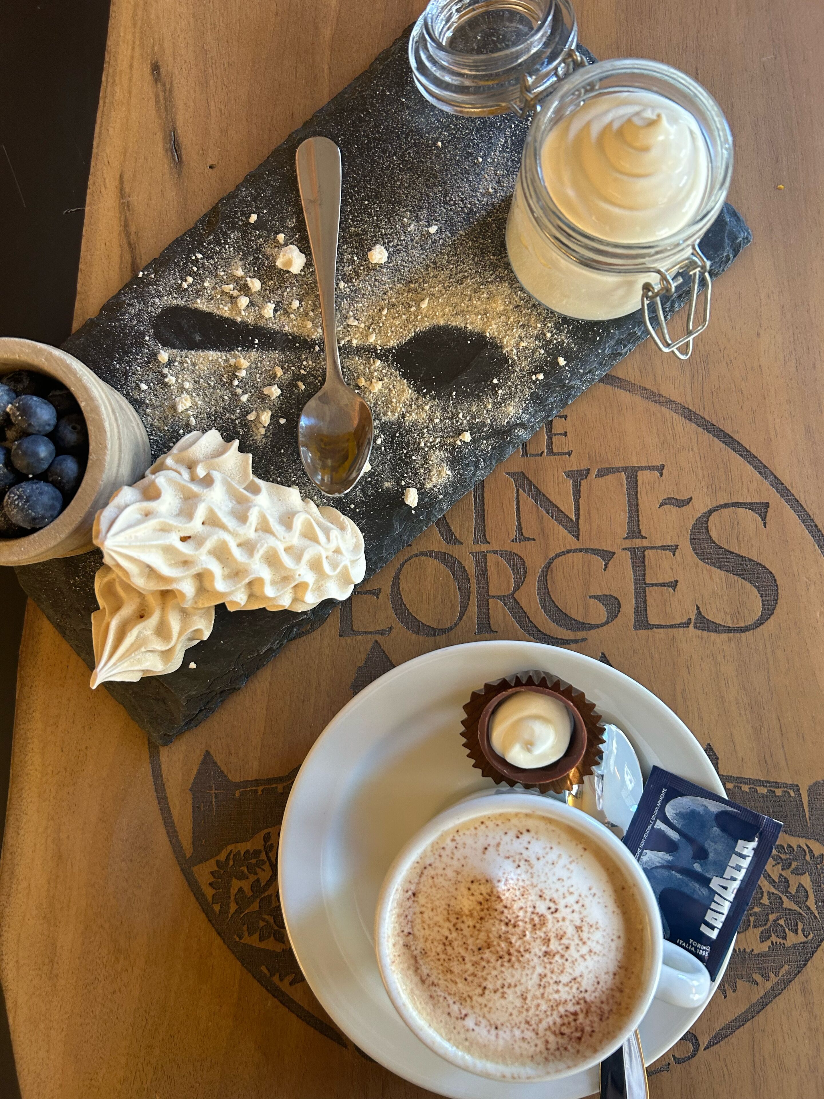 A dessert tray with whipped cream, a jar of cream, and a plate with a chocolate dessert and a coffee drink.