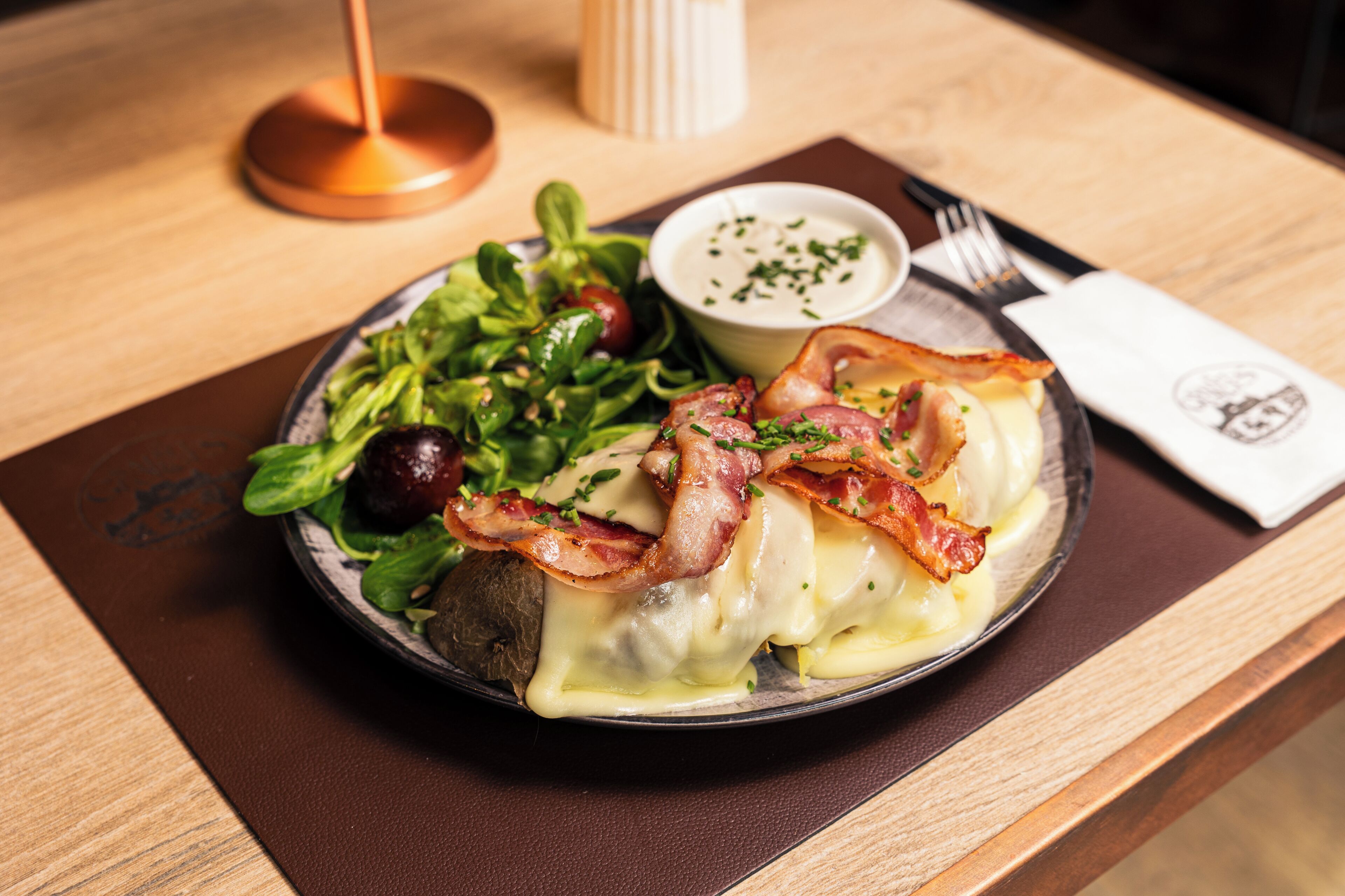 A plate of food with greens, cherry tomatoes, and bacon on a wooden table.