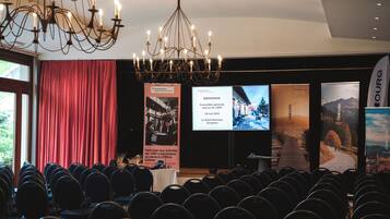 A conference room with rows of chairs, a chandelier, and banners with event information.