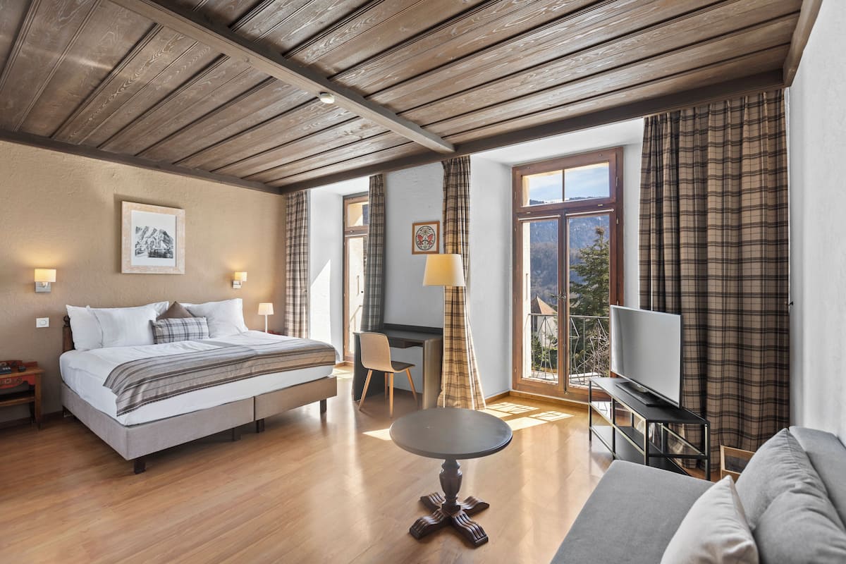 A spacious bedroom with a bed, a desk, a television, and a balcony view.