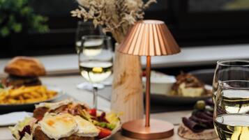 A dining table with various dishes and wine glasses, a lamp, and a view of mountains through a window.