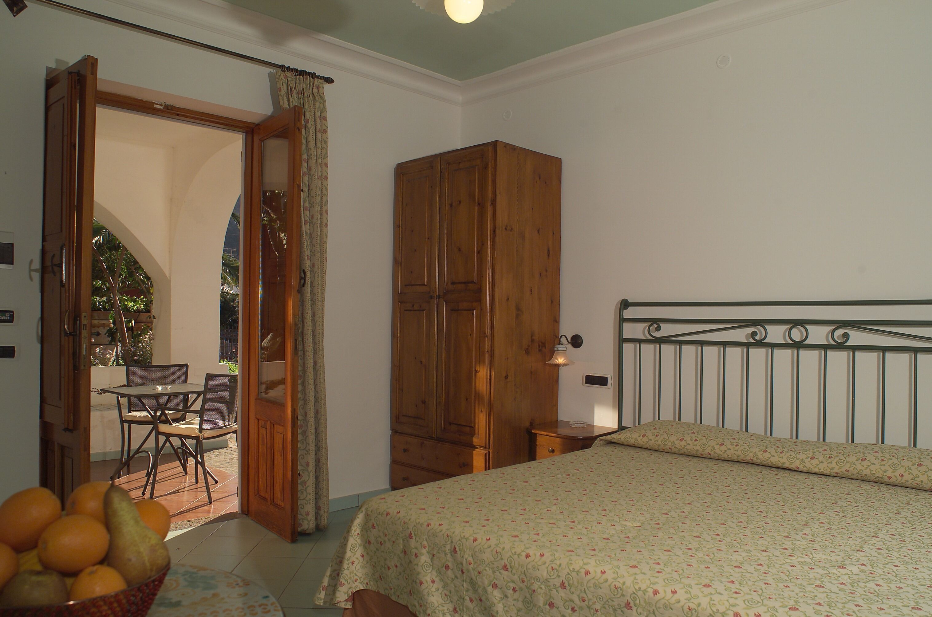 Une chambre à coucher avec un lit, une armoire en bois, une table avec des chaises et un panier de fruits.