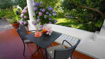 Un patio exterior con una mesa lista para dos personas, rodeado de exuberante follaje y plantas florecientes.