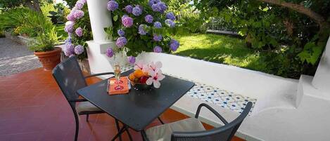 Un patio exterior con una mesa lista para dos personas, rodeado de exuberante follaje y plantas florecientes.