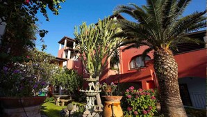 A courtyard with a fountain, palm trees, and a building with red walls. - Villa Fiorentino (Lipari)