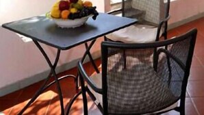 A patio with a table and chairs, a bowl of fruit, and a view of a garden with a fountain. - Villa Fiorentino (Lipari)