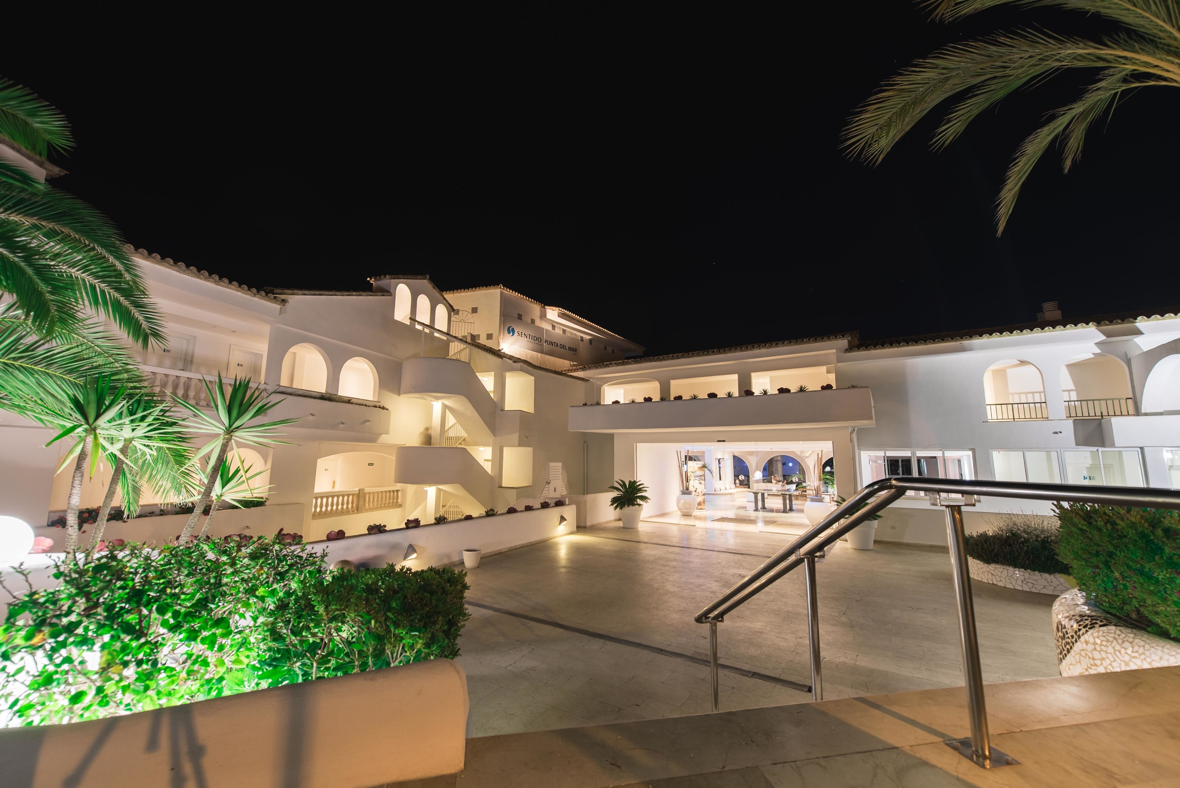 Un hotel de varios niveles con un patio central, palmeras y una escalera.