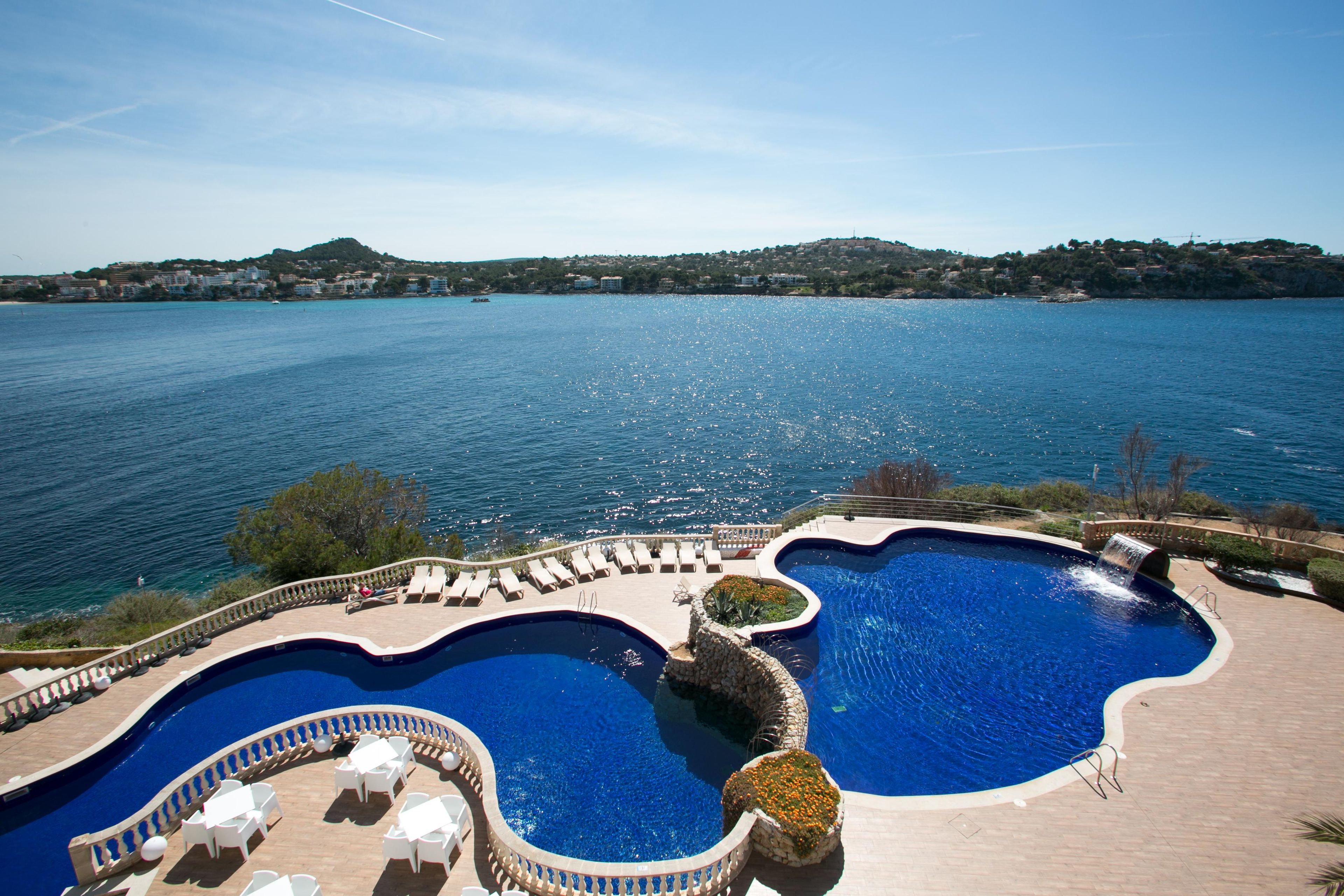 A pool area with multiple swimming pools, lounge chairs, and a view of the sea.