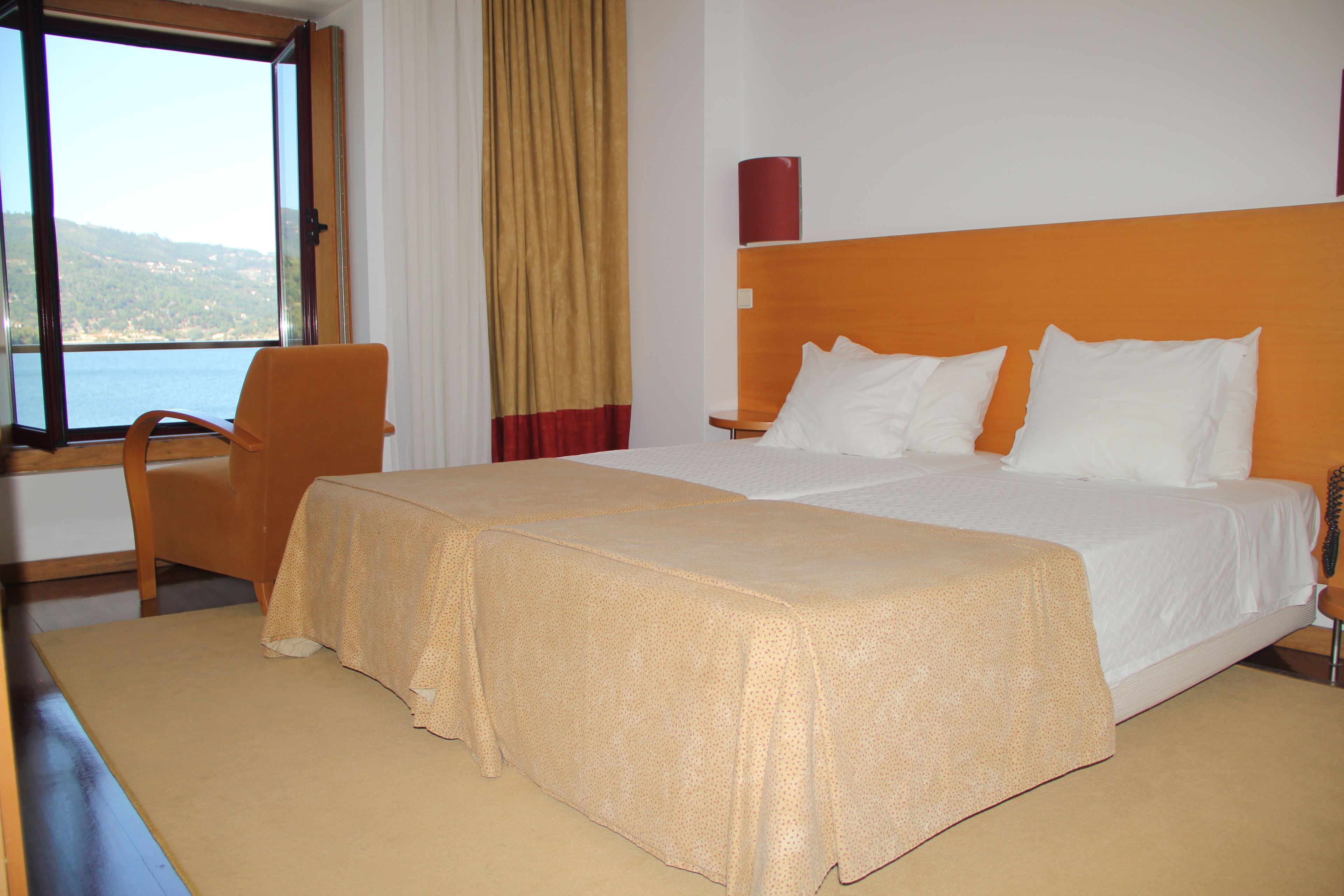A hotel room with a large bed, a chair, a table, and a window with a view of the sea.